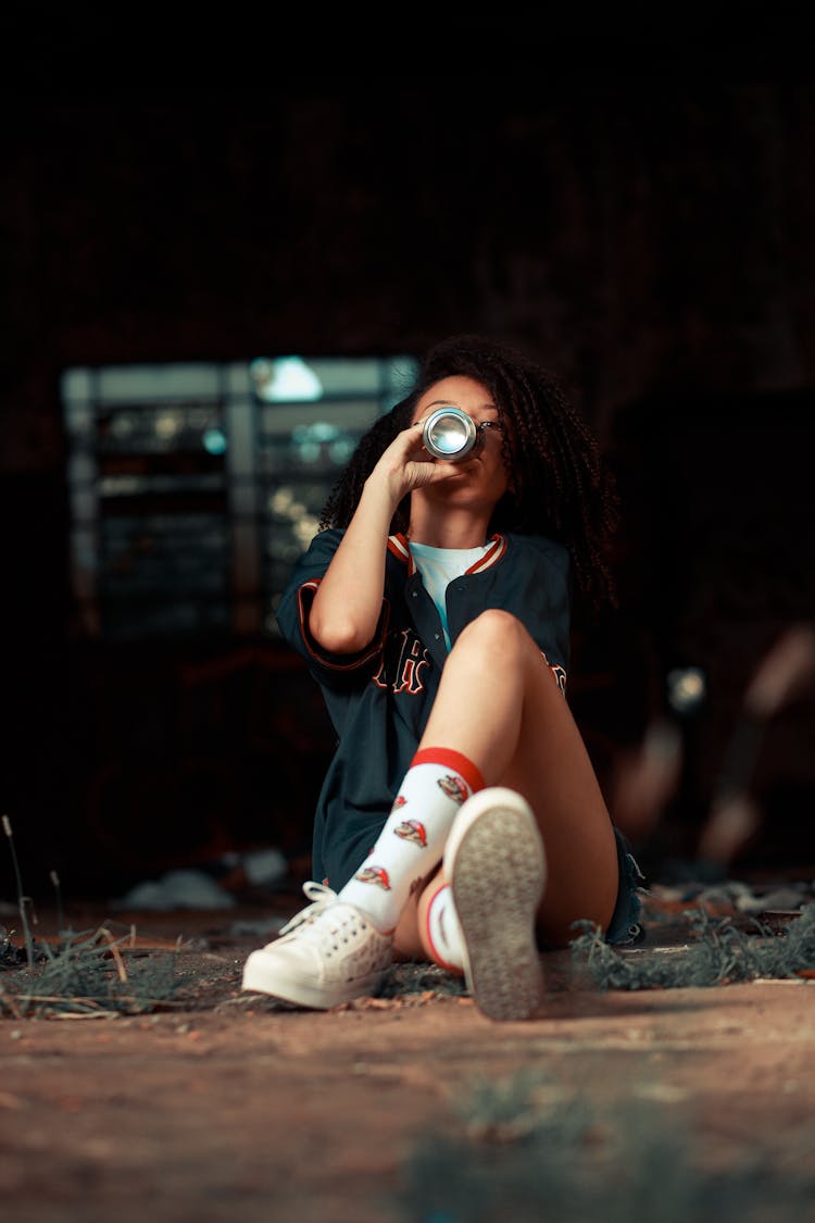 Woman Sitting On Ground And Drinking Energy Drink