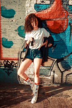 Stylish young woman in casual outfit posing against colorful graffiti wall.