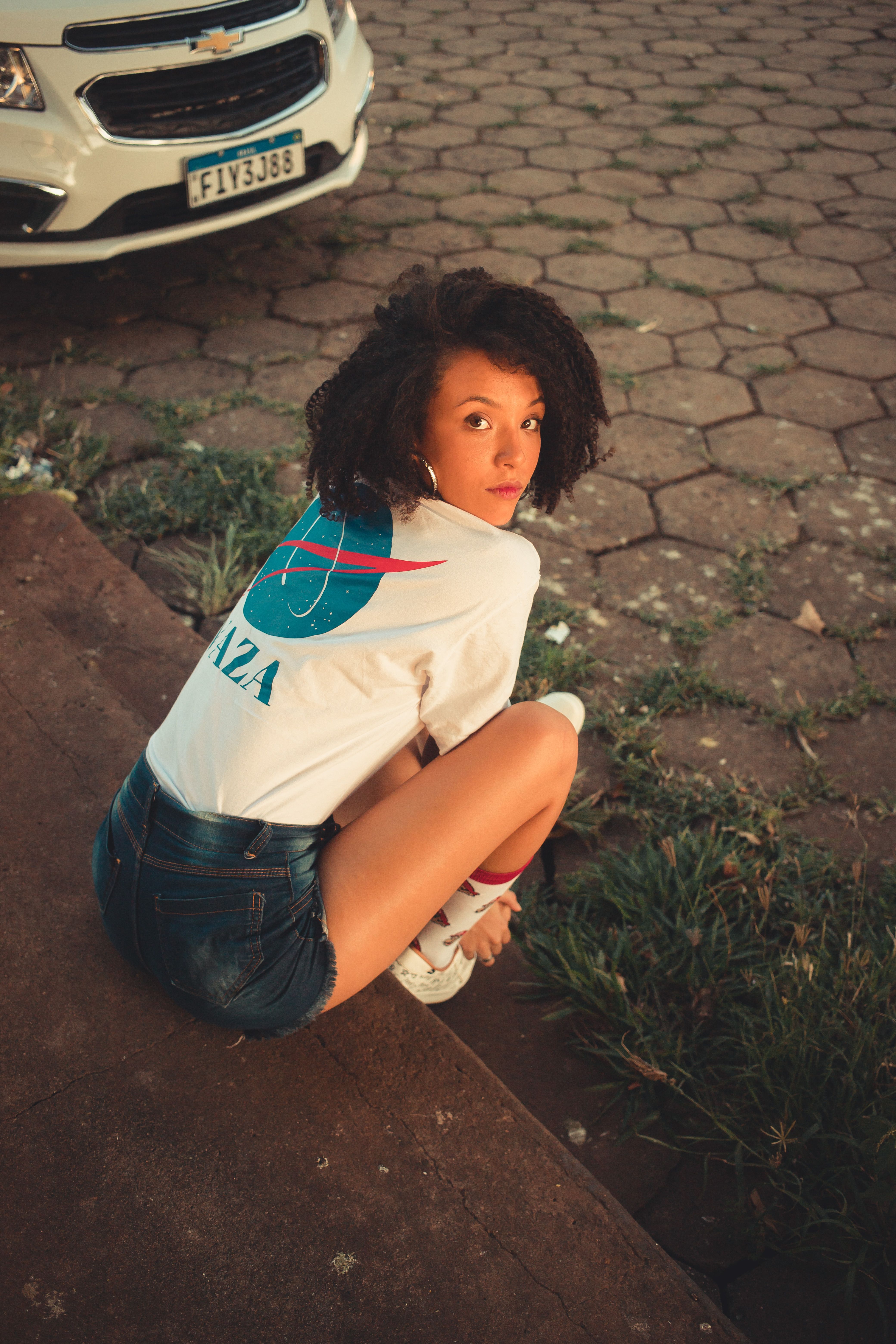 Young woman in denim shorts sitting outdoors, looking back confidently.