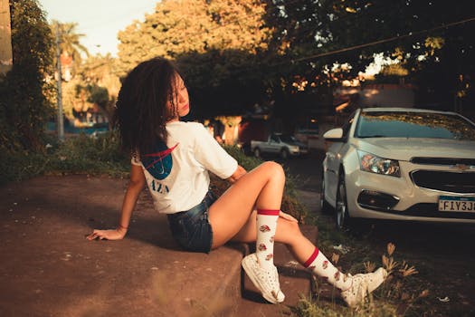 Young woman posing casually outdoors, showcasing trendy summer street fashion with a white car in the background.