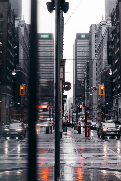 Free A bustling city street on a rainy day showcasing high-rise buildings and reflections. Stock Photo