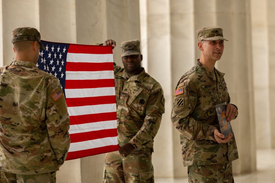United States Army soldiers in camouflage uniforms holding an American flag between marble columns