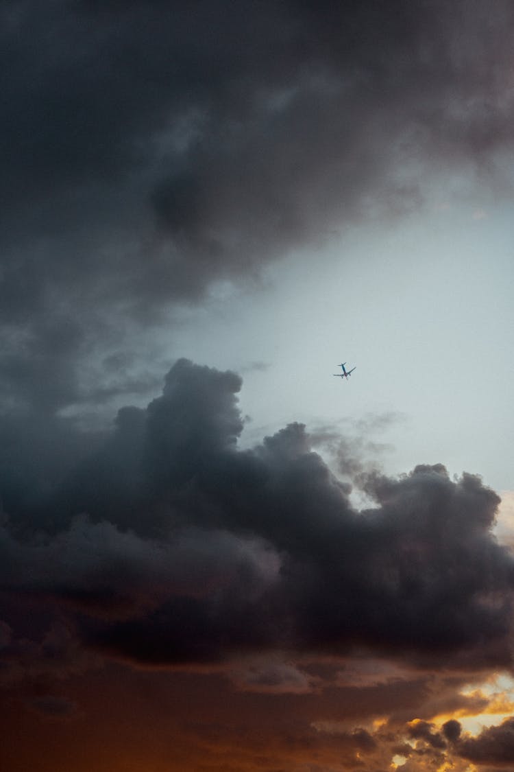 Airplane In Sky Between Dark Clouds