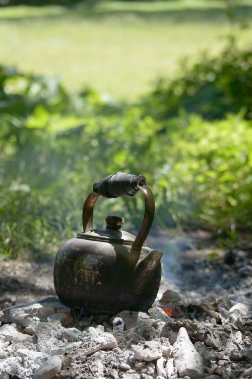 Free A vintage kettle heats over a campfire with smoke in a lush green outdoor setting. Stock Photo