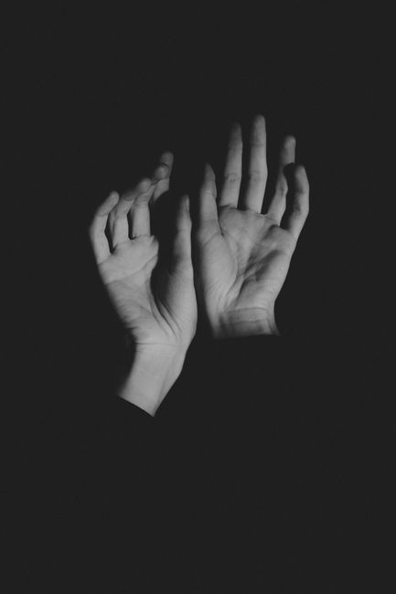 Artistic black and white close-up of human hands with a dark background.