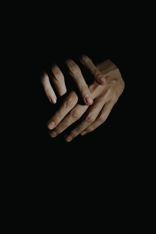 Free Close-up of hands intertwined in a dark setting, highlighting texture and emotion. Stock Photo