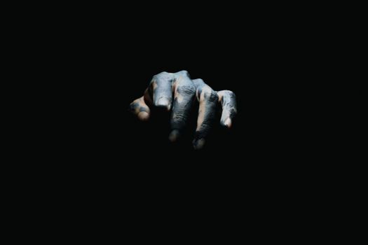 A tattooed hand extends out of the shadows on a black background, creating a mysterious atmosphere.
