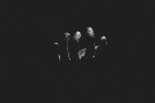 A monochrome image of a hand reaching out from darkness, evoking mystery.
