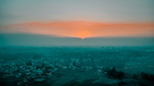 A stunning aerial view of a city at sunrise, shrouded in morning fog creating a serene ambiance.