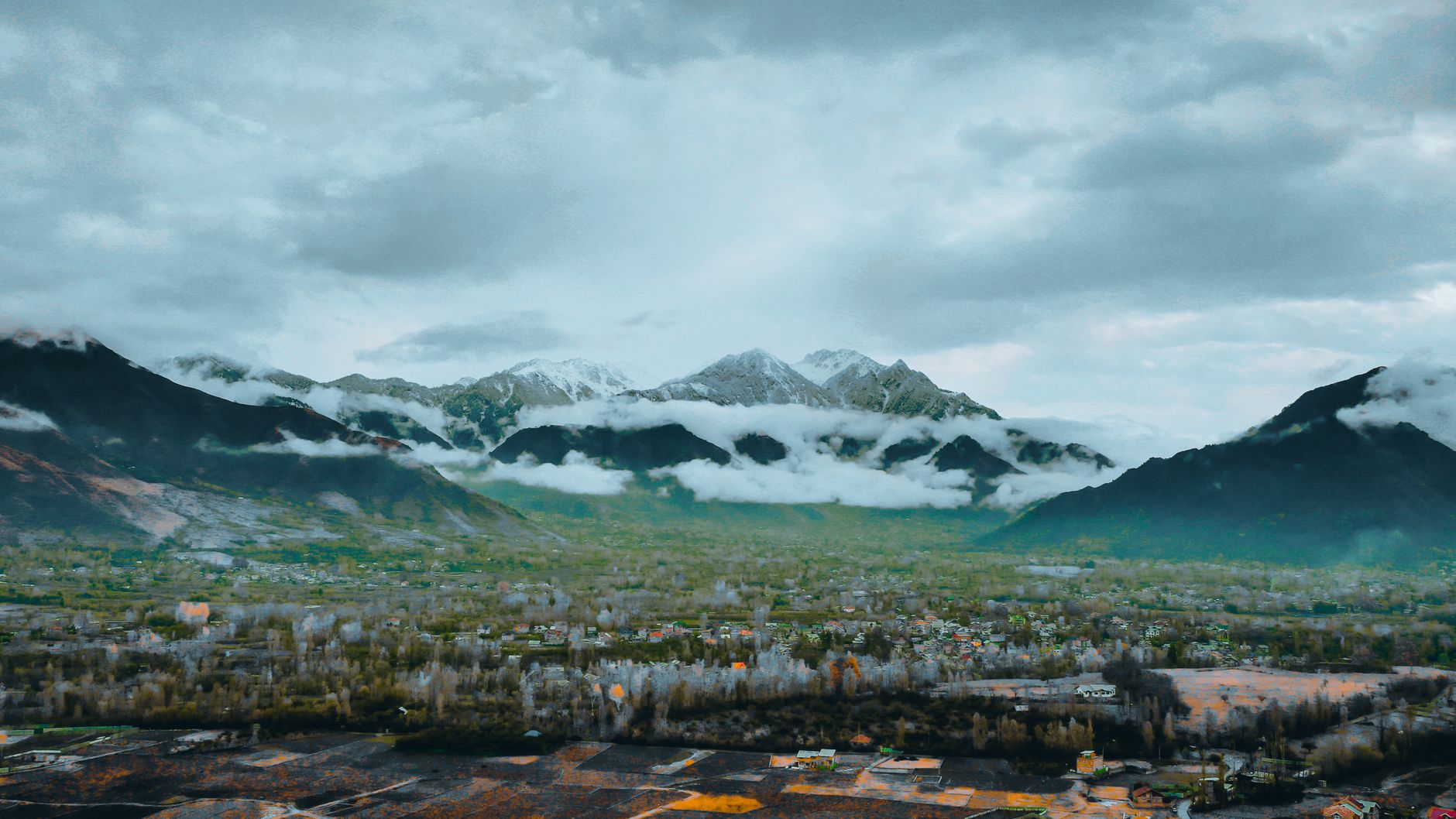 Stunning view of snow-capped mountains with fog over a lush green valley.