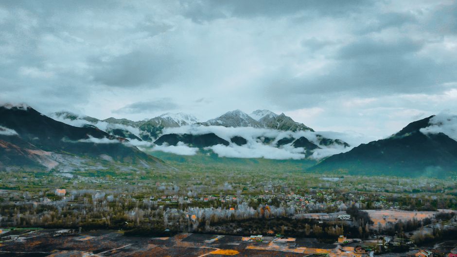 Stunning view of snow-capped mountains with fog over a lush green valley.