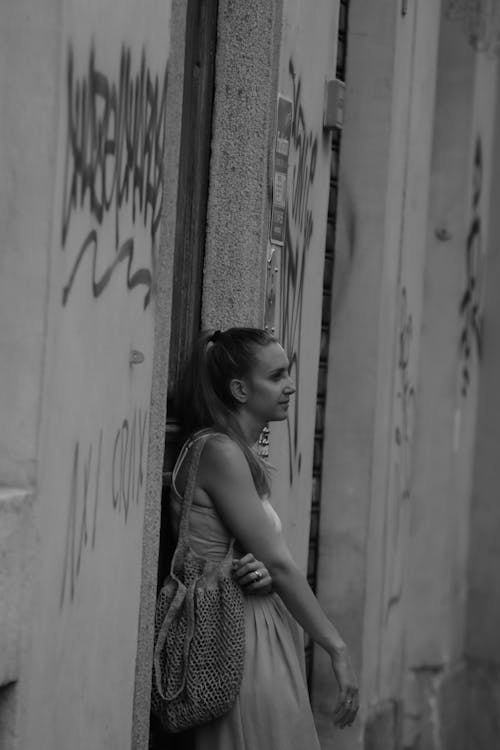 Grayscale Photo of Woman in Sleeveless Dress Leaning on Wall