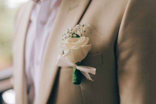 Free Close-up of a classic white rose boutonniere on a groom's beige suit jacket, symbolizing elegance. Stock Photo