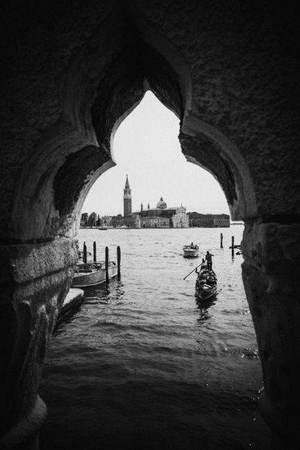Artistic black and white photograph of a gondola on Venice Lagoon, framed by historical architecture.