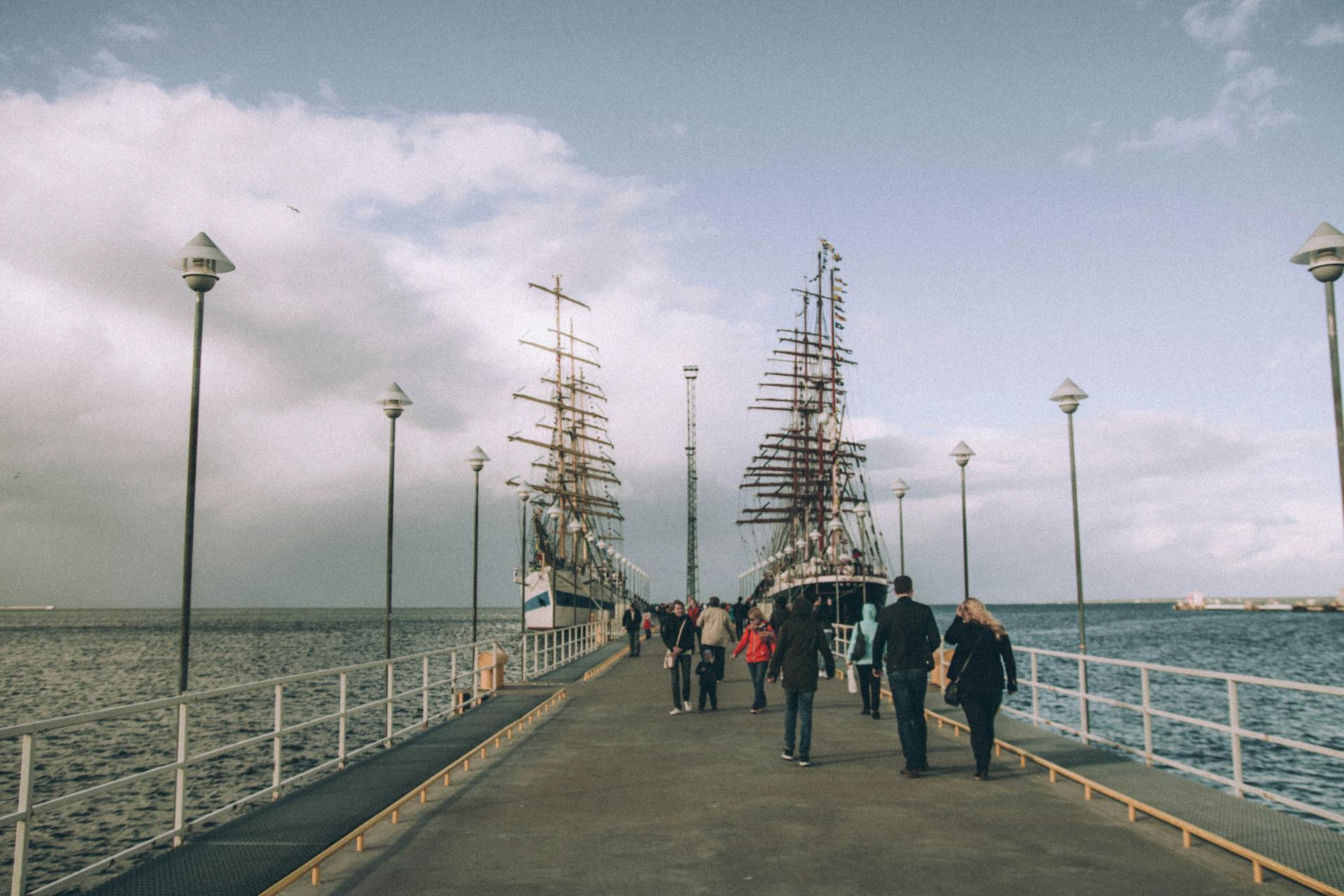 A tranquil pier scene with tall ships and tourists under a cloudy sky, ideal for travel themes.