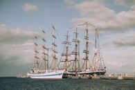 Sailing ships near pier with people under cloudy sky