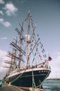 Sailing ship with Russian flag located near wharf with people admiring vessel with big deck decorated with flags of different countries in cloudy day