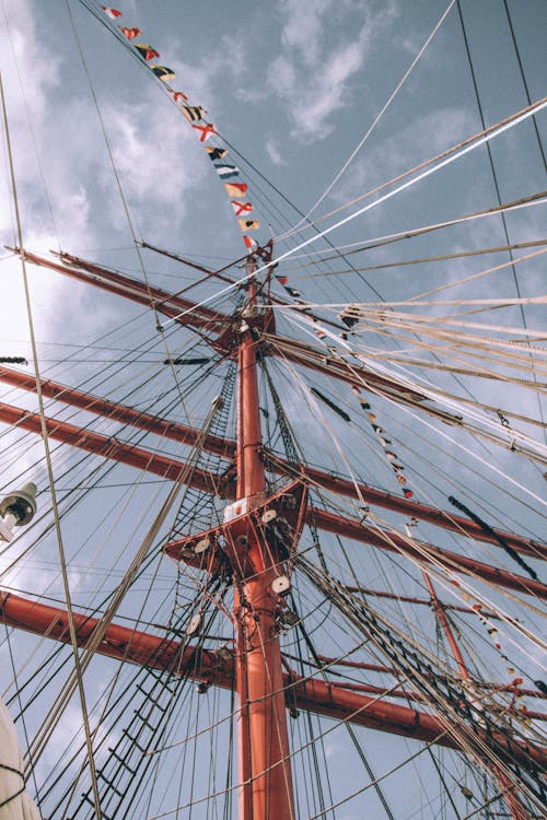 From below of modern metal mast with guy lines sustaining construction and rope decorated with different countries flags against cloudy blue sky