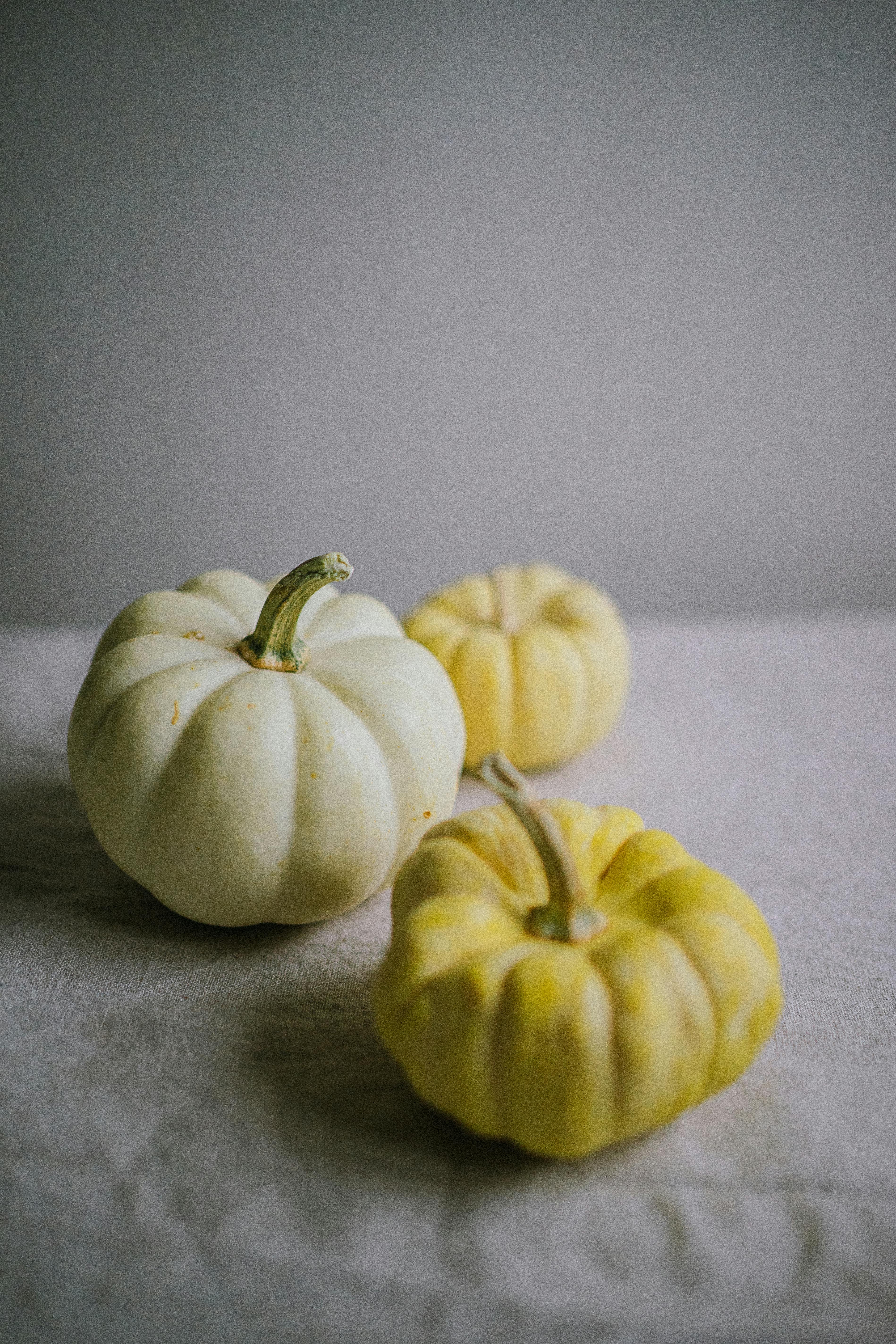 Aesthetic composition of white and yellow pumpkins on a textured linen surface, perfect for autumn themes.