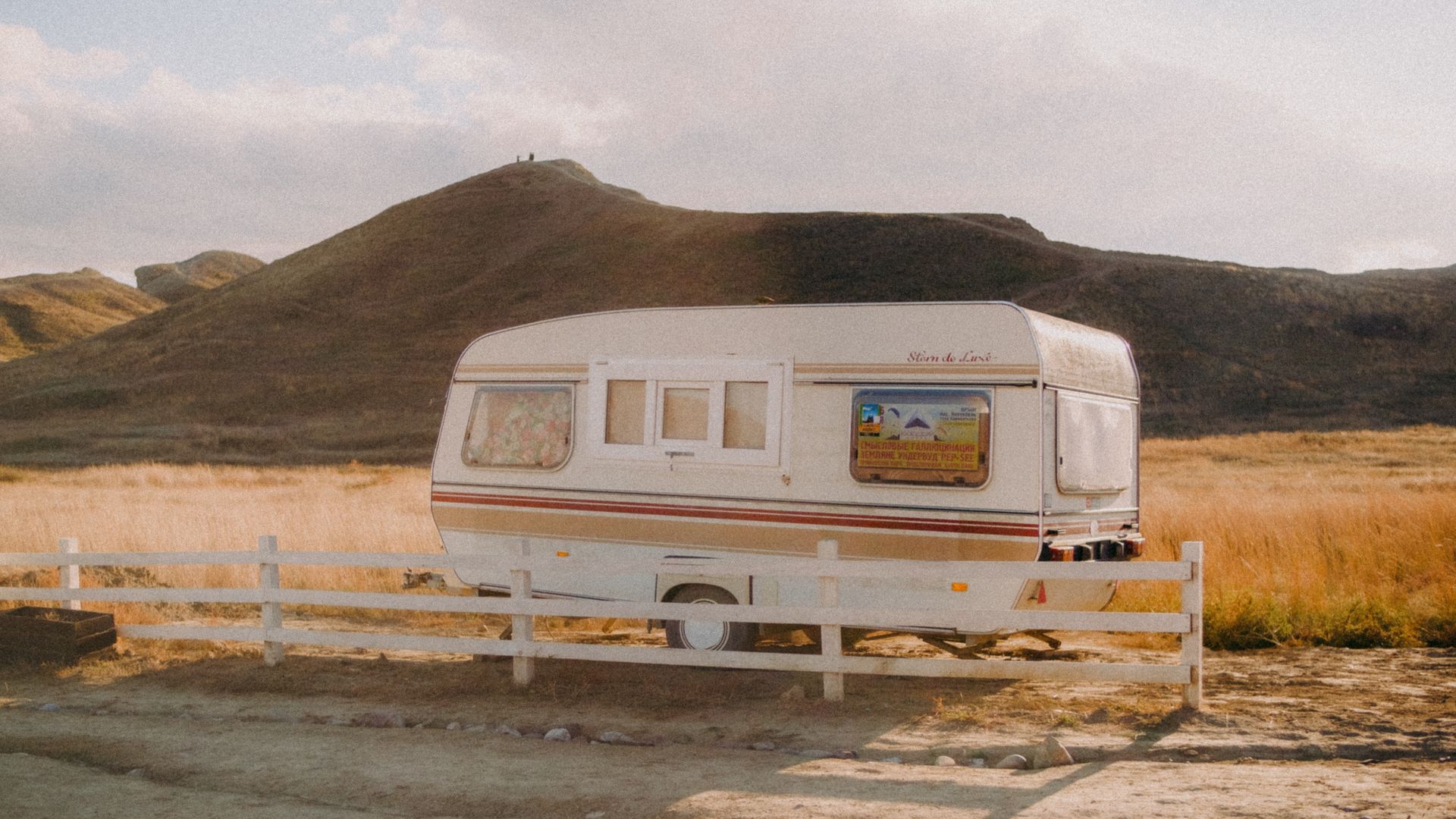 A vintage camper parked in a serene field against mountainous hills, capturing a peaceful travel vibe.