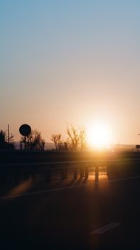 Sunset view over a highway with silhouetted trees and a glowing horizon.