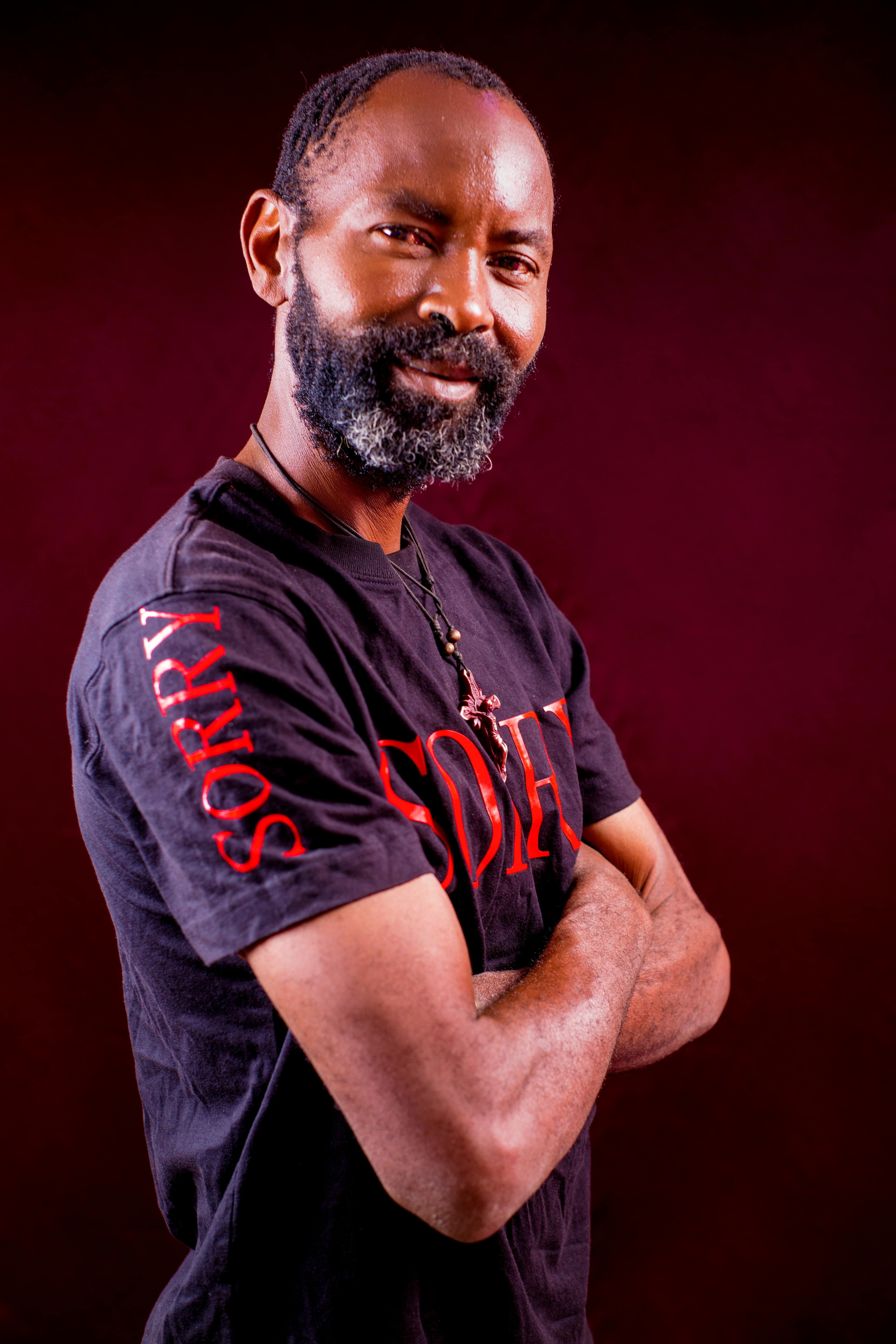 Man with beard and arms crossed wearing a statement T-shirt posing confidently.