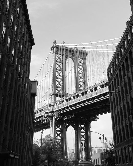 Black and white view of Manhattan Bridge framed by buildings in New York City.