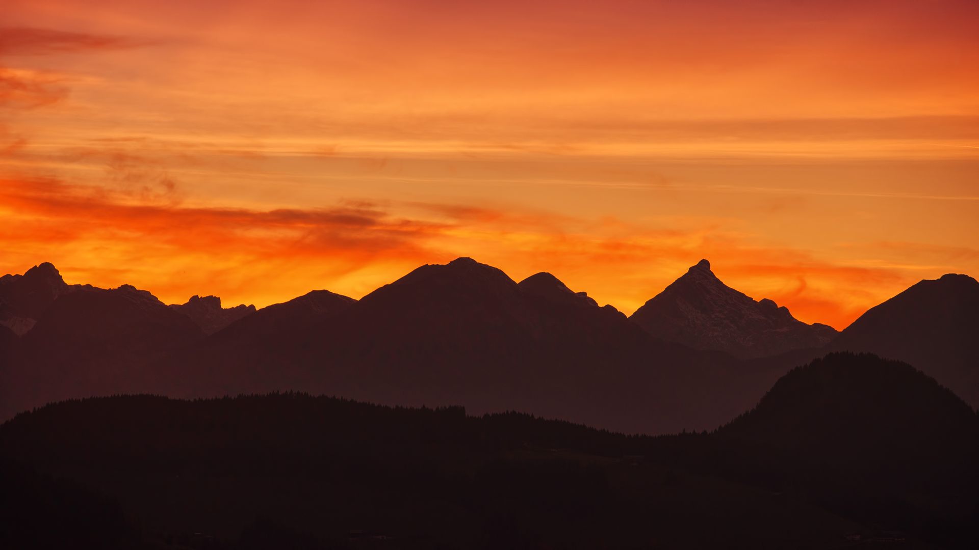Silhouette of mountains against a vibrant orange sunrise sky. Perfect for nature enthusiasts.