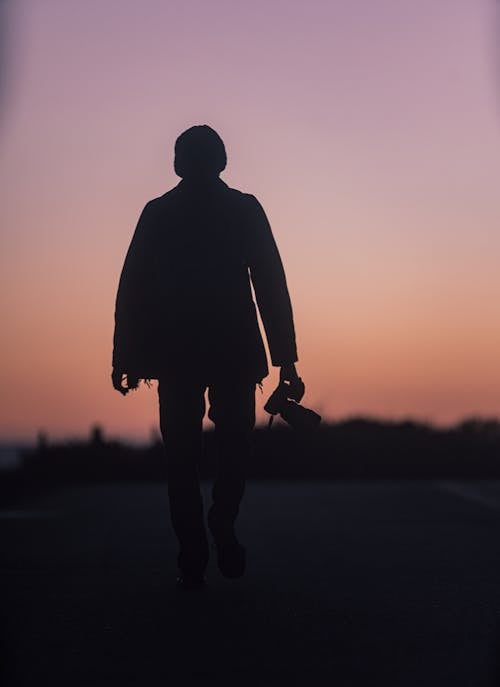 Silhouette of a Man Walking with a Camera in His Hand at Sunset 