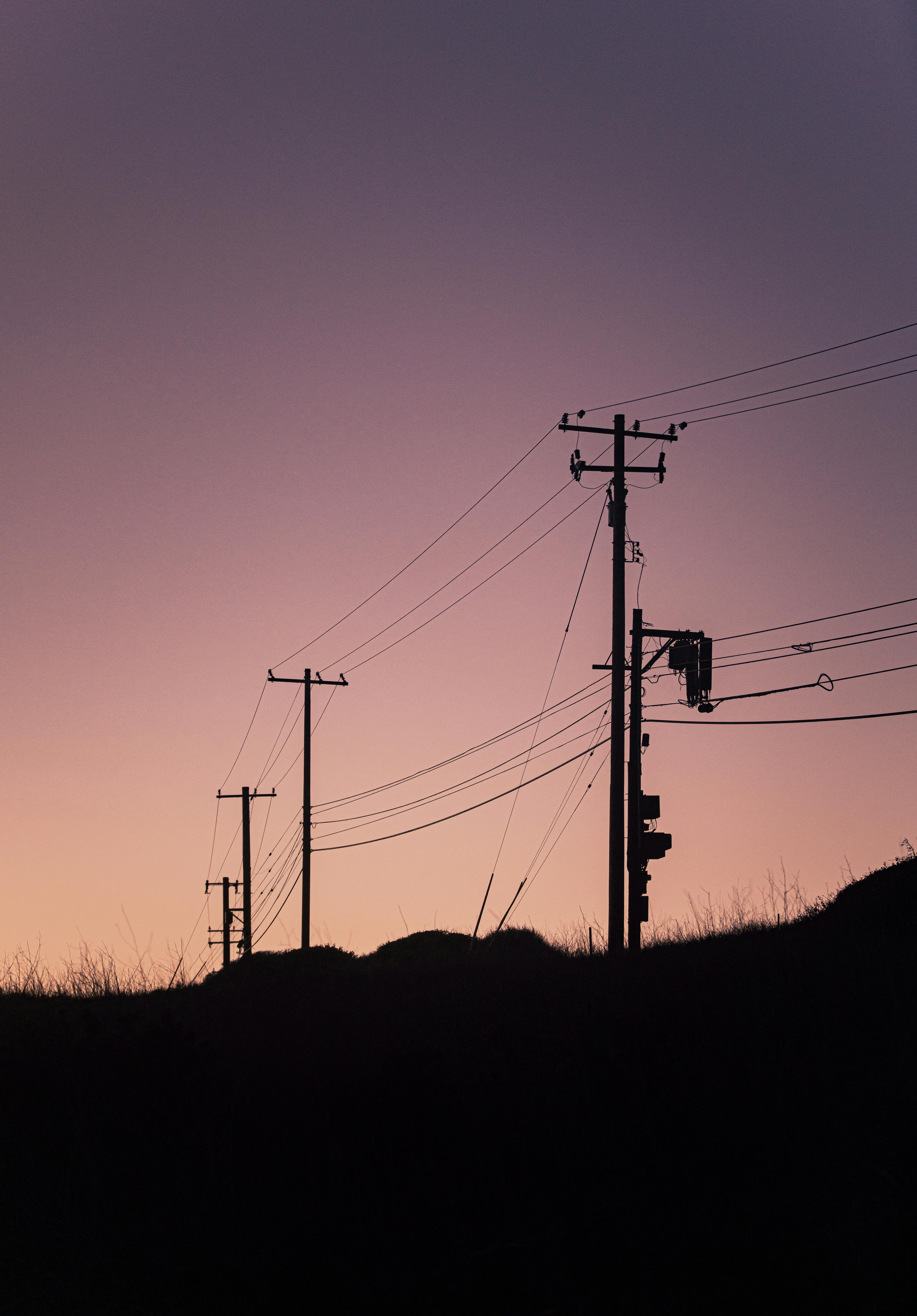 Electric poles silhouette against a vibrant sunset sky with dramatic hues.