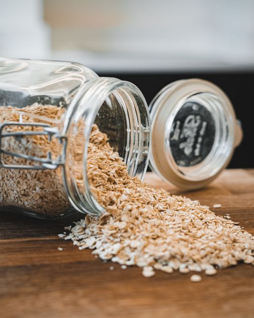 Free Oats spilling from a glass jar on a wooden surface creating a rustic kitchen scene. Stock Photo