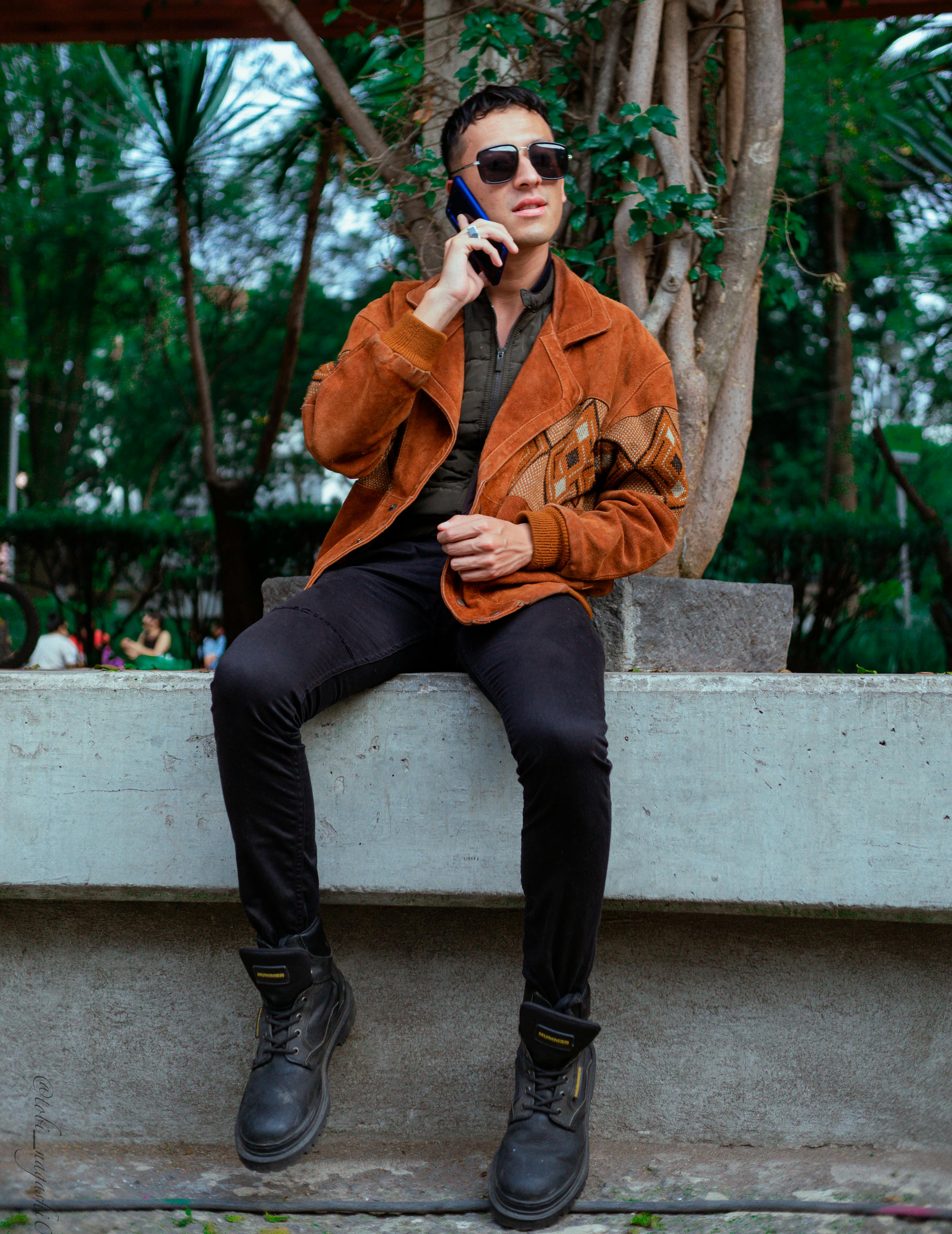 man in brown jacket and black pants sitting on white concrete bench