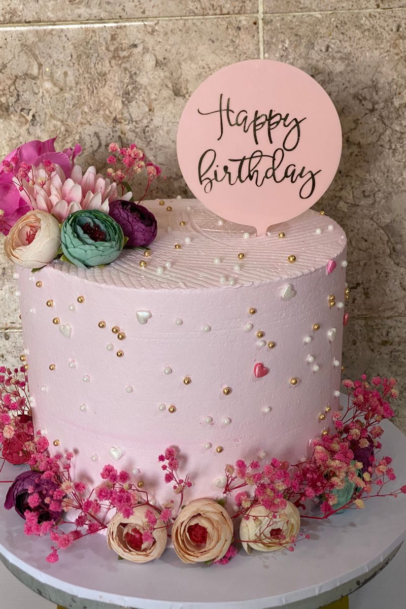 Pink birthday cake topped with flowers on a festive table