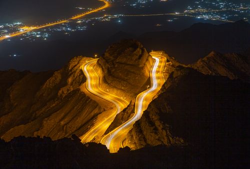 Free Captivating aerial shot of a winding highway with light trails through rocky mountains at night. Stock Photo