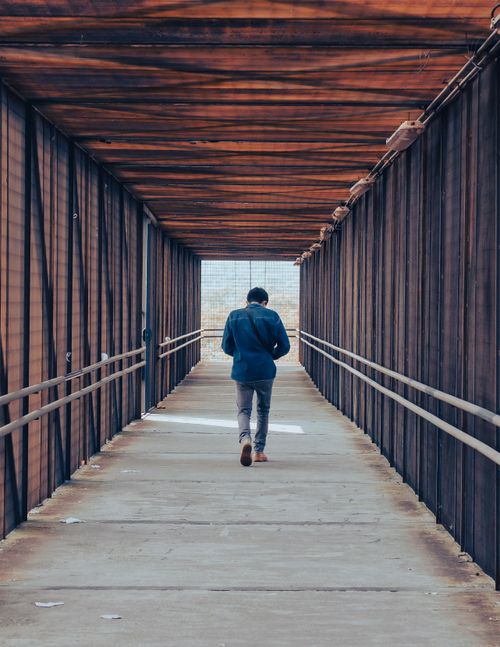 Free A man walks alone on a wooden covered bridge in an urban environment, captured from behind. Stock Photo