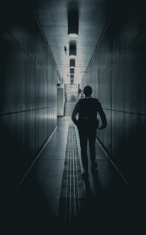 Free A silhouette of a man walking in a dark, narrow underground tunnel towards the light. Stock Photo