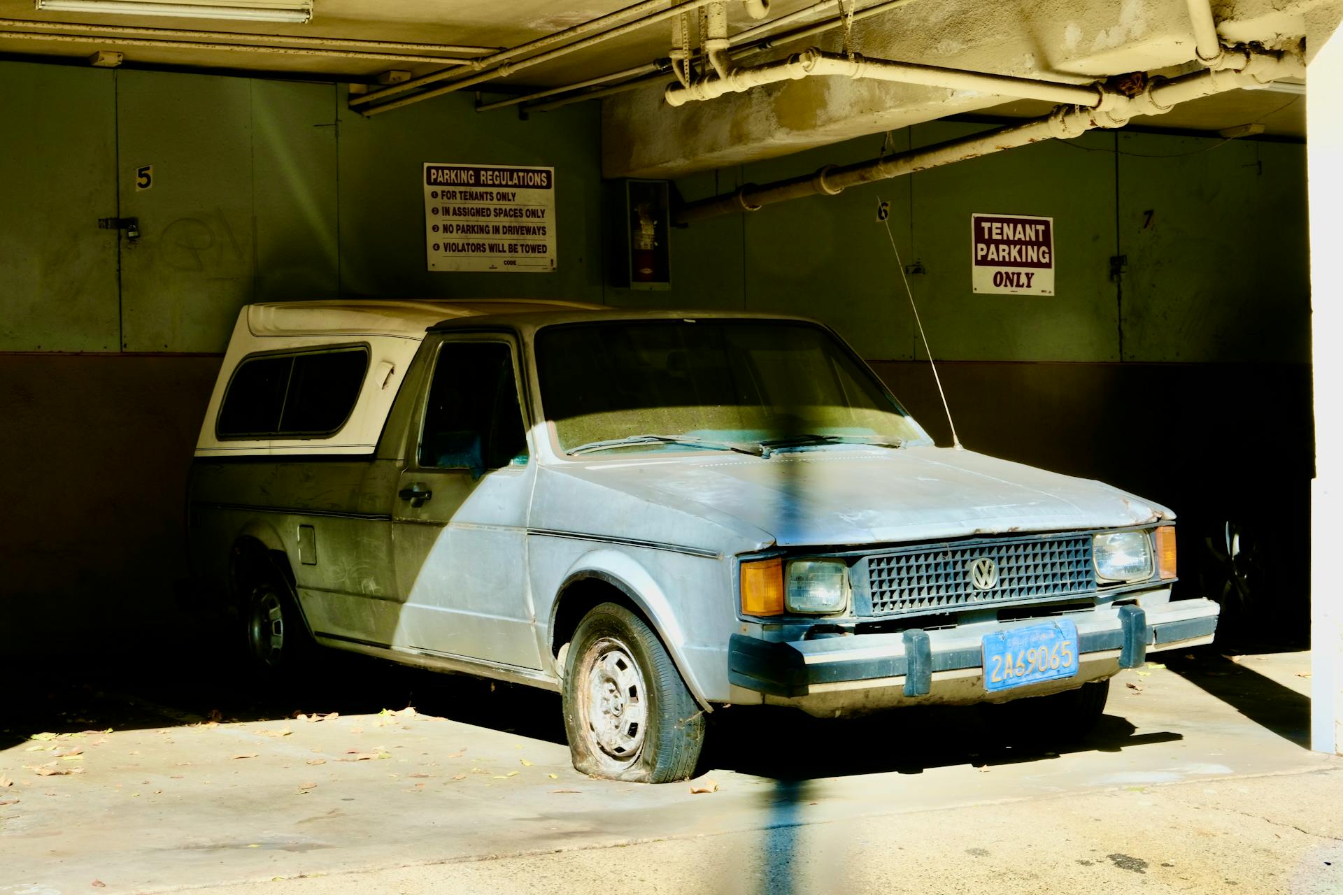 A vintage Volkswagen truck with flat tires parked in an abandoned garage, showcasing urban decay.