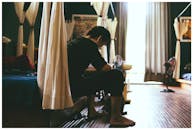 一名亚洲男子坐在阳光明媚的室内房间里，周围挂着窗帘