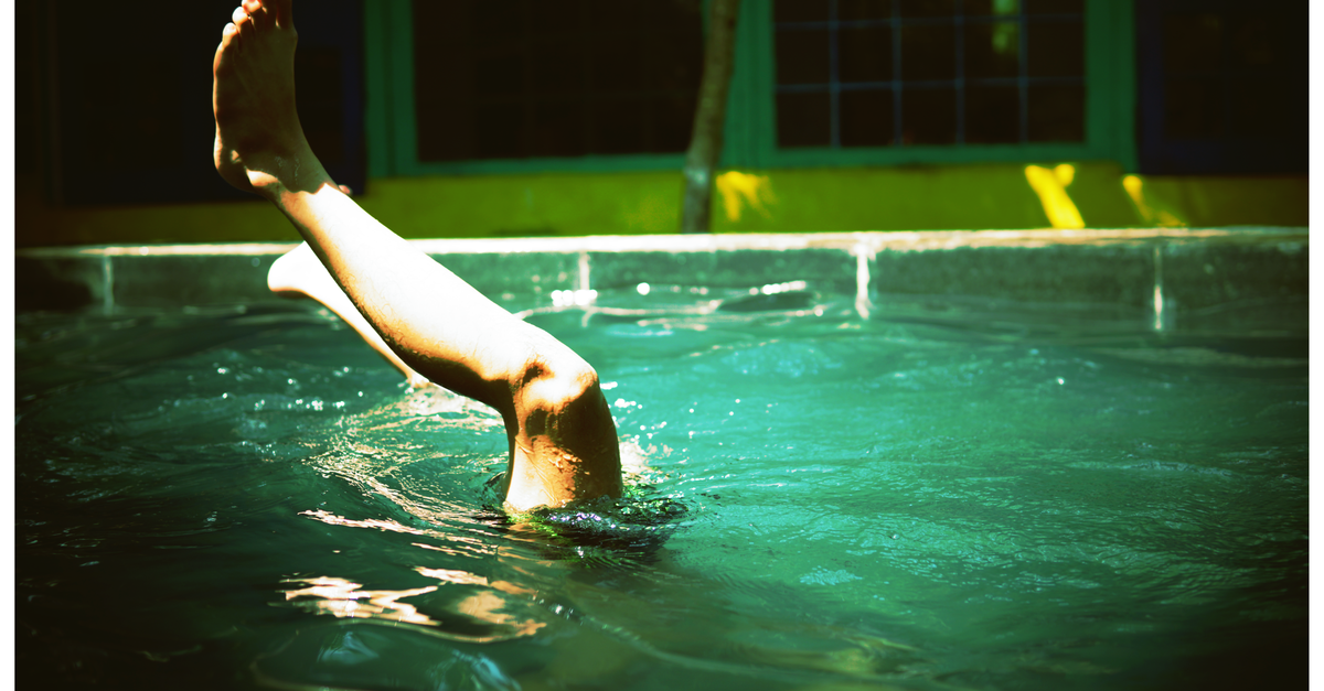 A close-up of a swimmer's leg emerging from water in a sunlit pool outdoors.