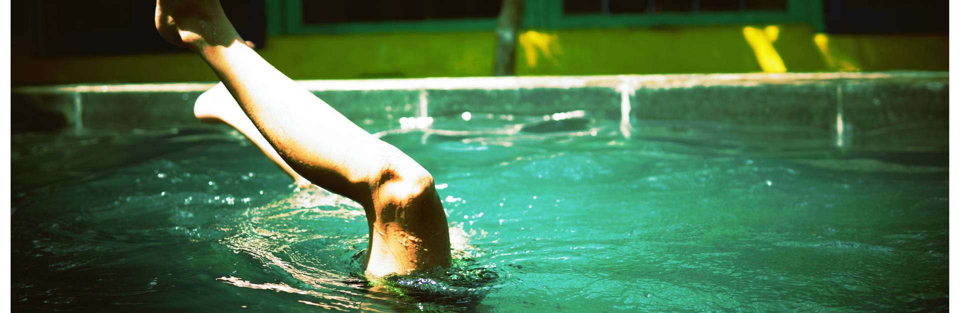 A close-up of a swimmer's leg emerging from water in a sunlit pool outdoors.