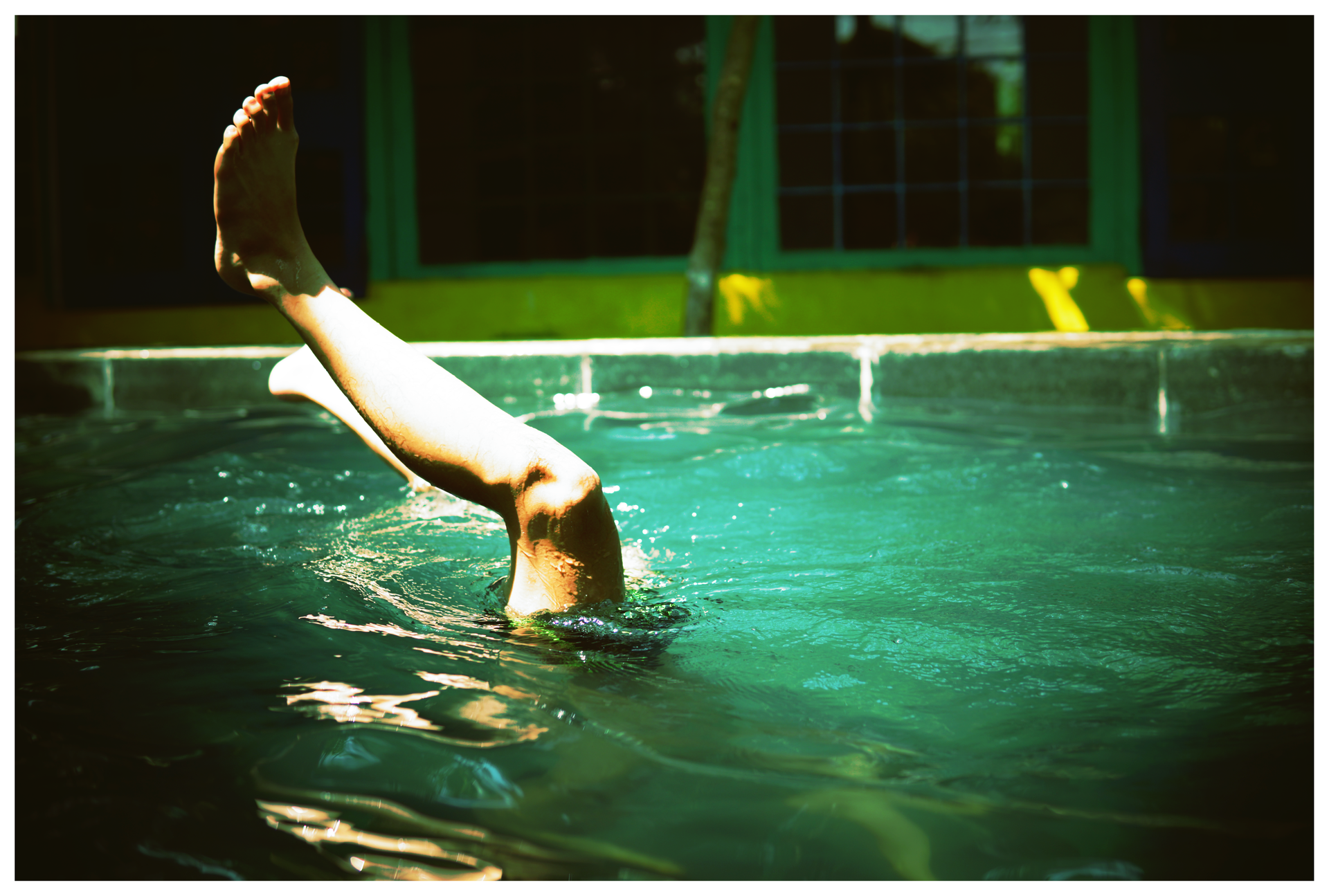 A close-up of a swimmer's leg emerging from water in a sunlit pool outdoors.