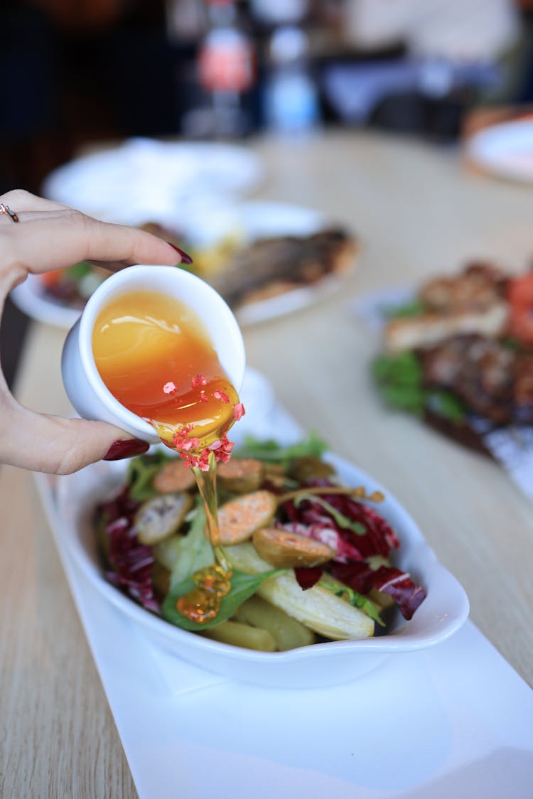 A Person Pouring A Dressing On A Salad