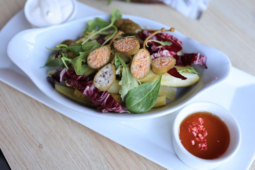 Vibrant mixed salad with fresh greens, figs, capers, and dressing, served in a white dish.