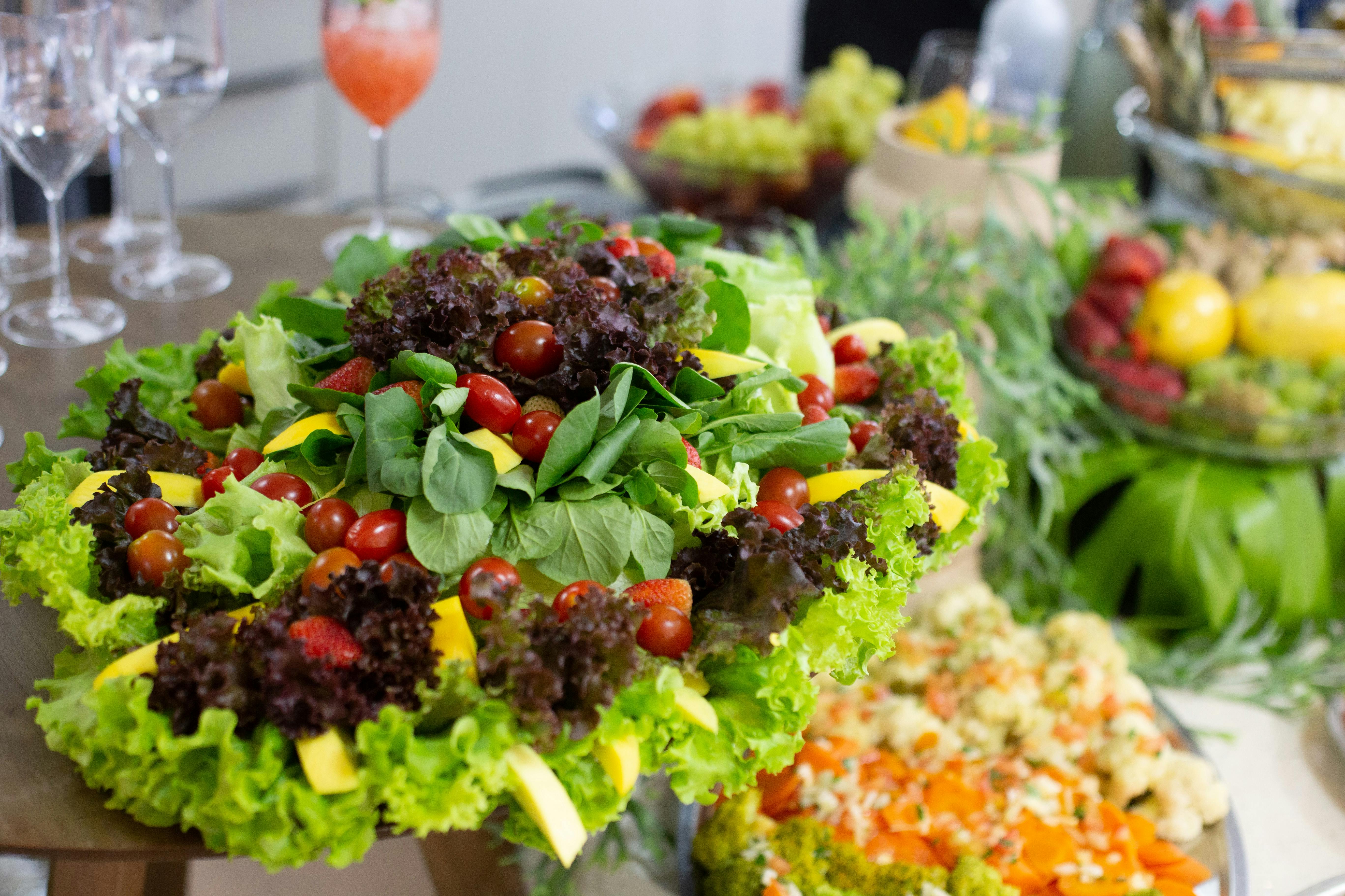 Colorful mixed salad with leafy greens, cherry tomatoes, and mango slices on a buffet table.