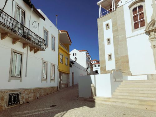 Free A quiet street in Lisbon showcasing traditional architecture under a clear blue sky. Stock Photo