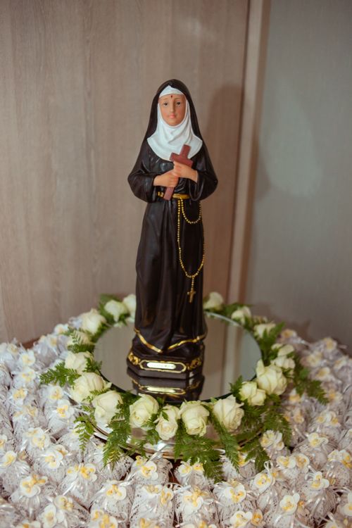 Free A nun figurine on a mirror, encircled by white flowers and rosary beads, symbolizing devotion. Stock Photo