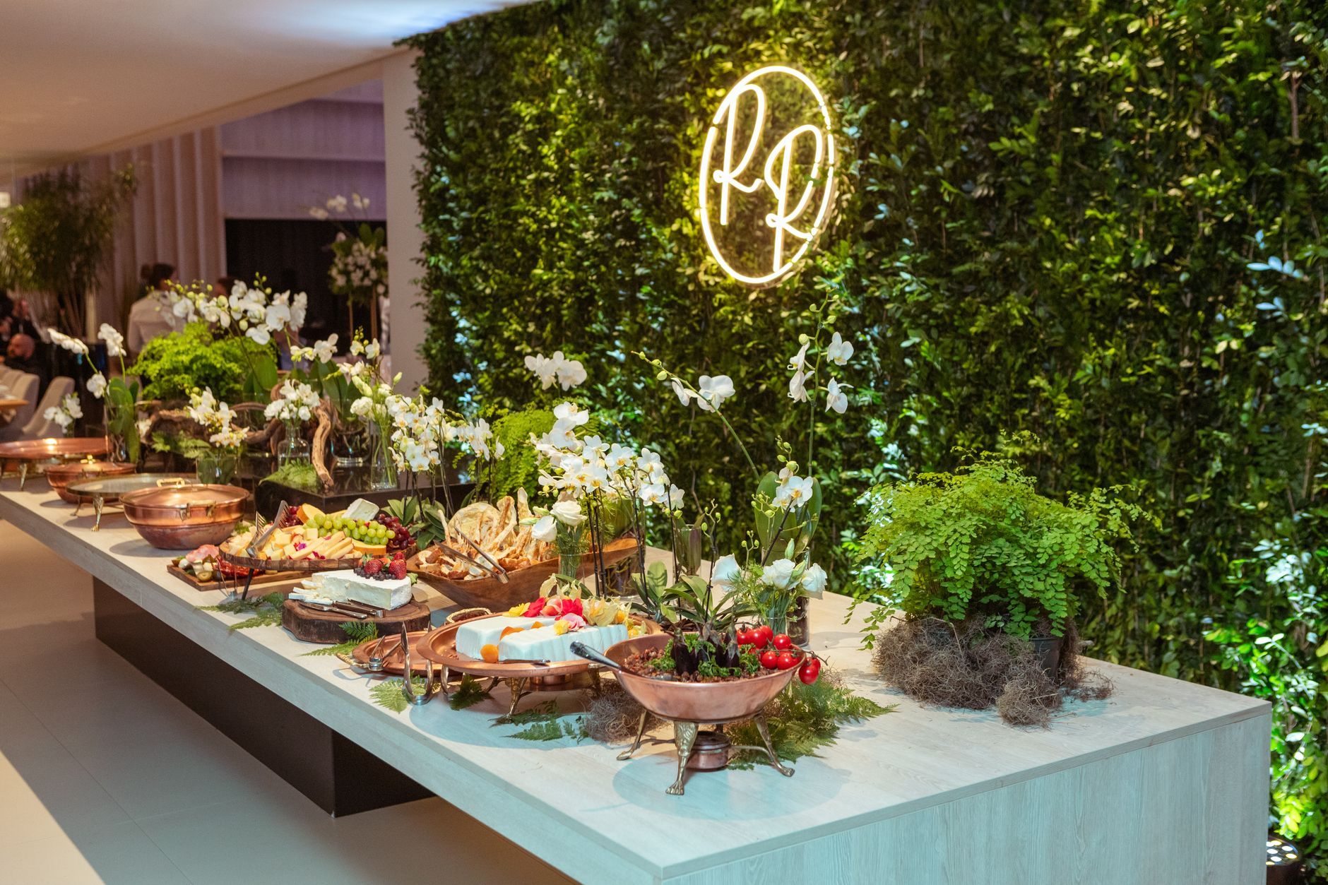 Lavishly decorated buffet table with food and flowers against a green wall backdrop.