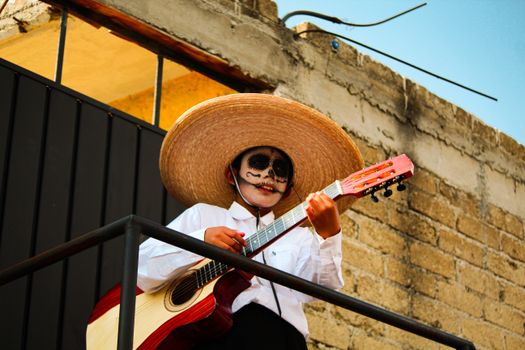 A child in face paint and sombrero playing guitar for Dia de los Muertos in Mexico.