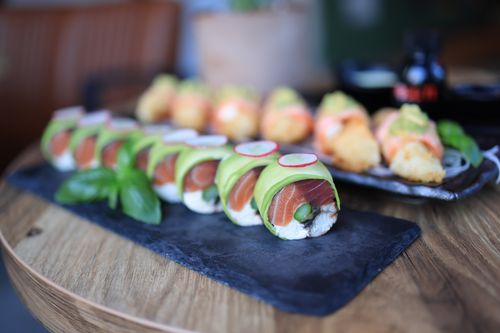 Free Close-up of sushi rolls with avocado and salmon, garnished with fresh basil on a slate platter. Stock Photo
