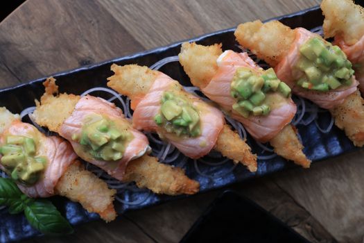 A close-up of tempura sushi with salmon and avocado, perfectly styled on a black plate.